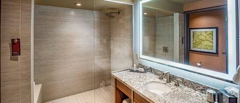 A modern bathroom with a glass-enclosed shower, a large mirror, and a marble countertop.