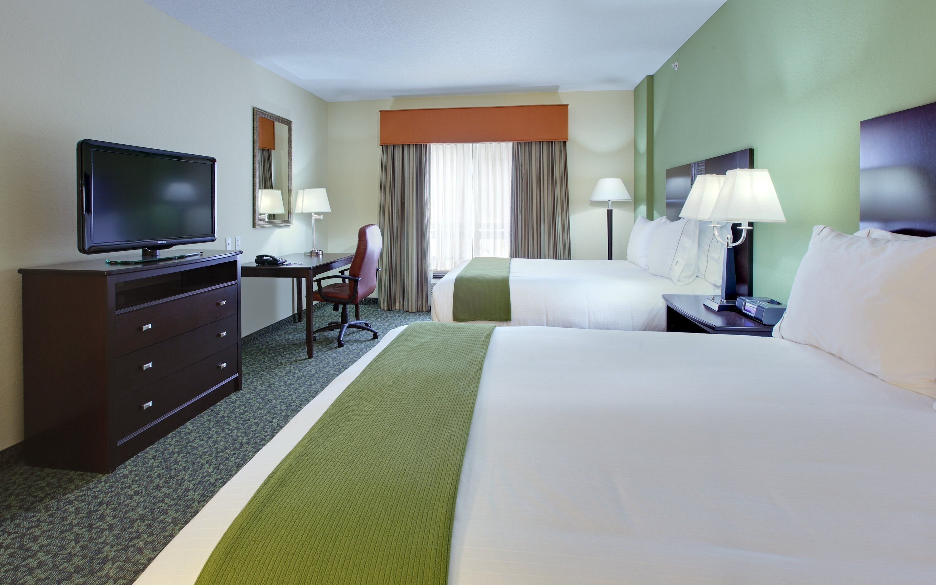 A hotel room with a bed, a desk, a chair, a television, and a lamp.