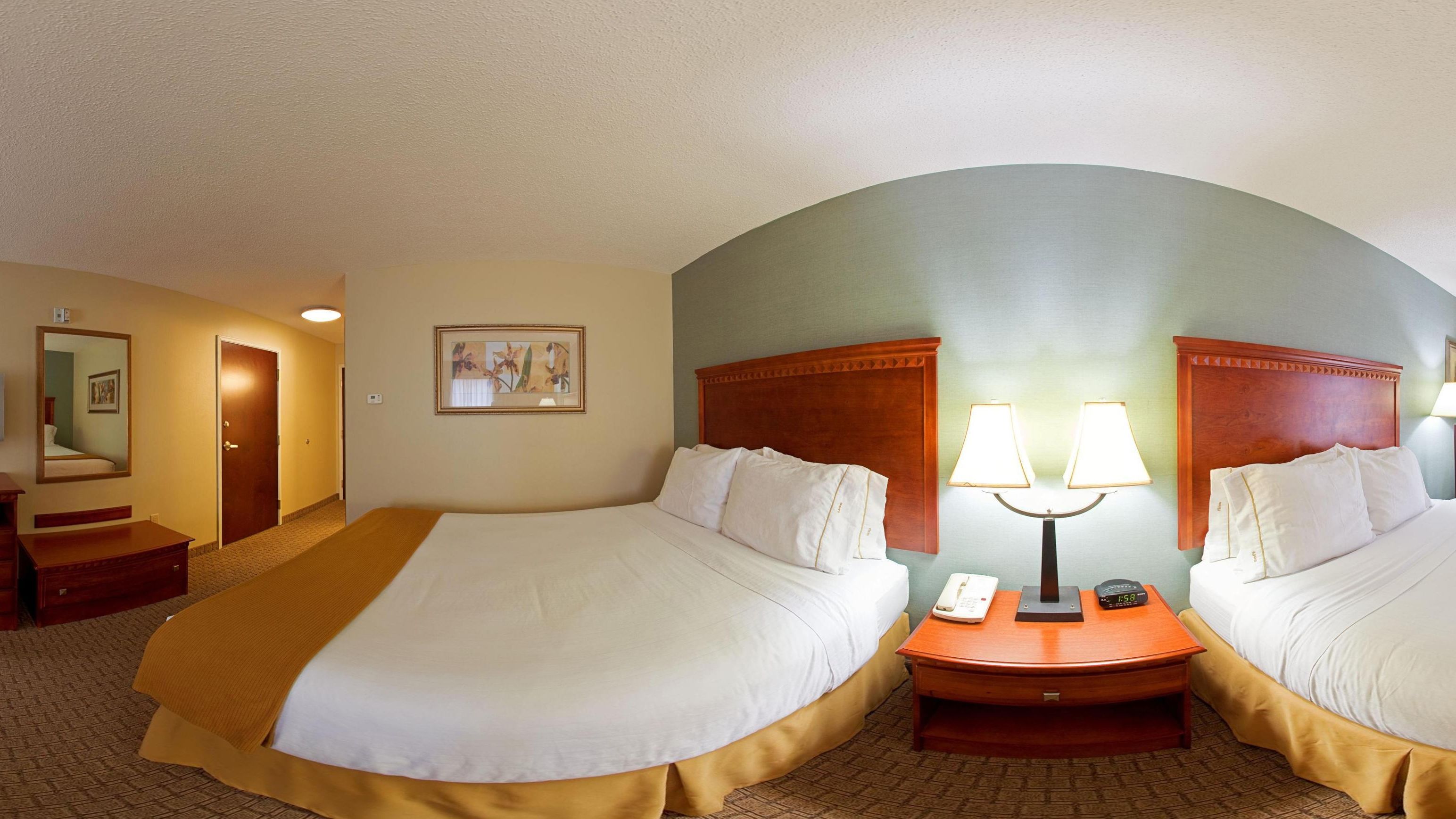 A hotel room with two beds, a bedside table with a lamp, a phone, and a clock.