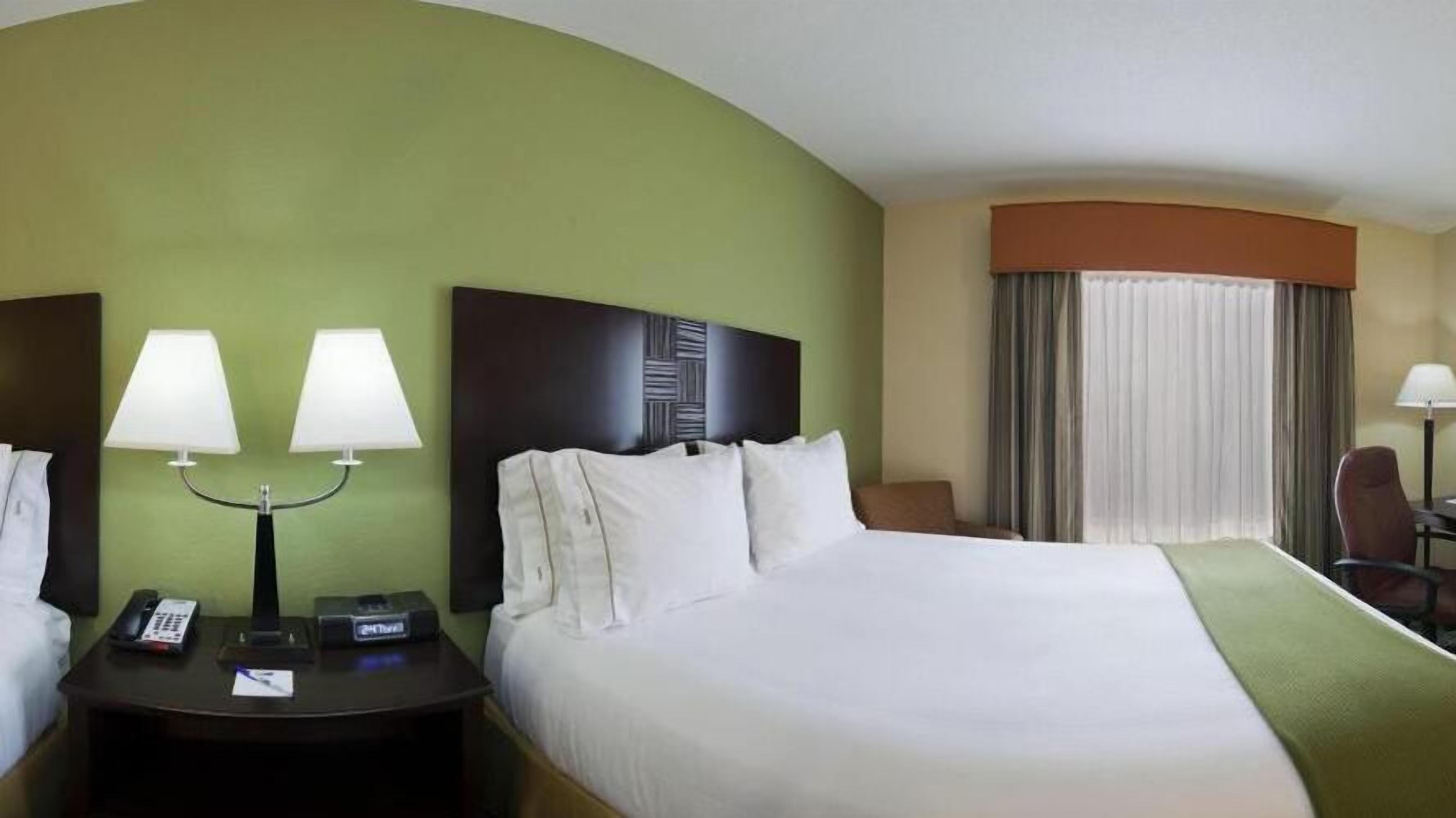 A hotel room with a large bed, two bedside tables with lamps, a telephone, and a chair.