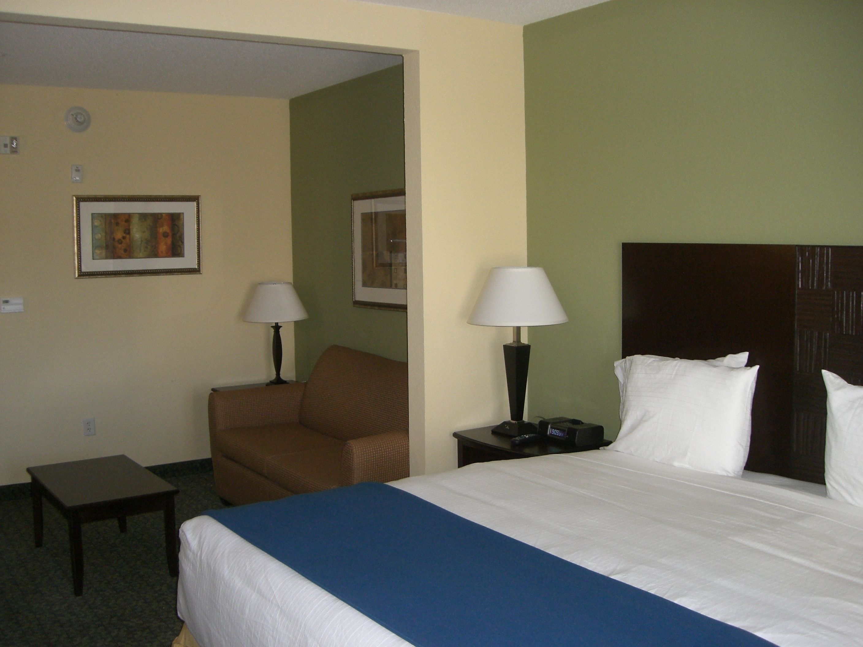 Una habitación de hotel con una cama, dos mesitas de noche, una silla, una pequeña mesa y dos lámparas.