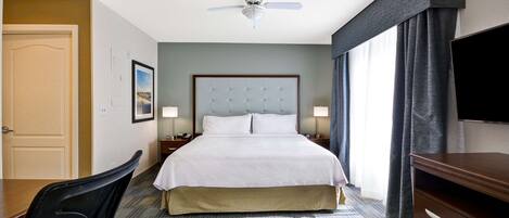 Ein Hotelzimmer mit einem Bett, einem Schreibtisch, einem Sessel, einem Fernseher, einem Deckenventilator und einem Fenster mit Vorhängen.