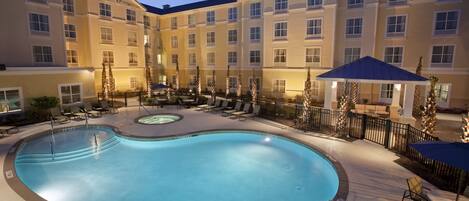A hotel courtyard with a swimming pool, lounge chairs, and a covered seating area.