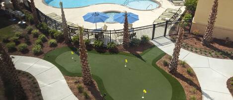 A pool area with a putting green, palm trees, and lounge chairs.