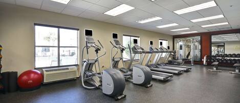 A gym with treadmills, elliptical machines, and a red exercise ball.