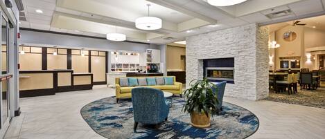 A lobby with a reception desk, a yellow sofa, a patterned armchair, and a large potted plant.