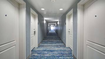 A hotel hallway with a patterned carpet, white doors, and recessed lighting.