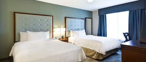 Habitación de hotel con dos camas, un escritorio, una silla, un ventilador de techo y una ventana con cortinas.