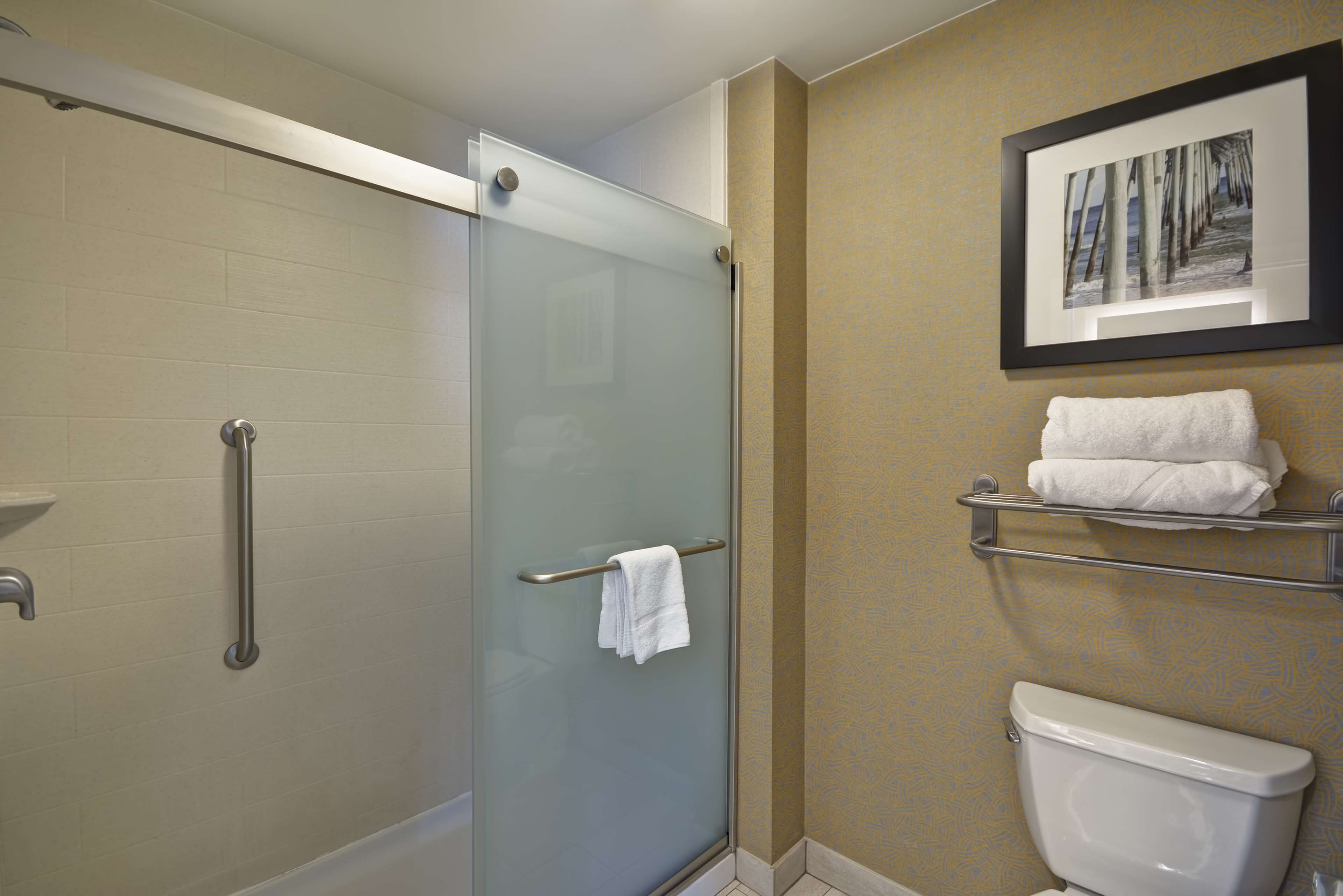 A bathroom with a glass shower enclosure, a white toilet, and a towel rack with towels.