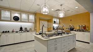 A modern kitchen with white cabinets, a central island with a glass enclosure, and overhead pendant lighting. - Homewood Suites Wilmington/Mayfaire (Wilmington)