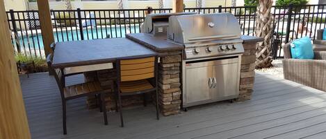 An outdoor barbecue area with a grill, a table, and chairs.
