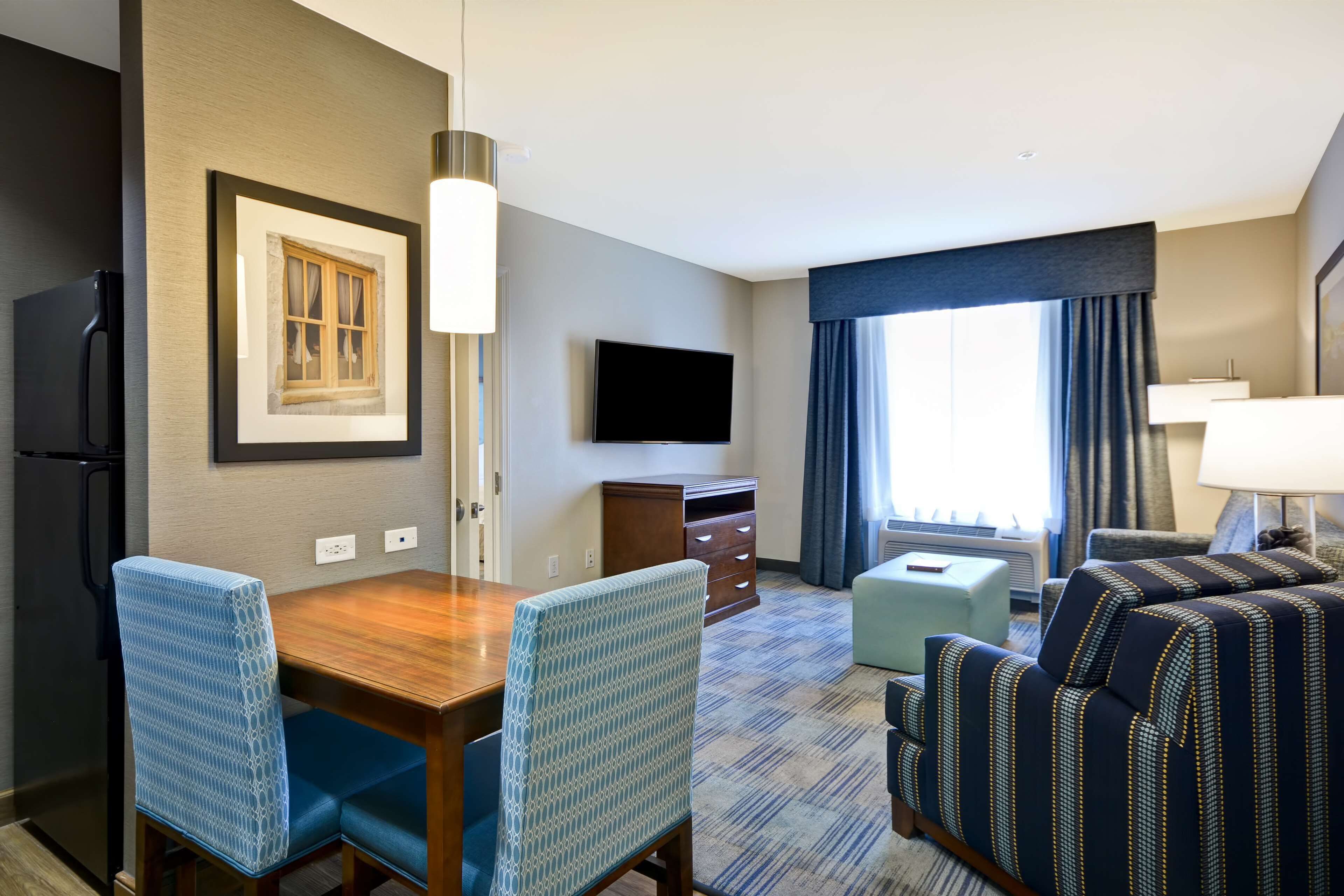 A hotel room with a dining table, chairs, a TV, a sofa, and a window with curtains.