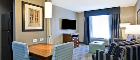 A hotel room with a dining table, chairs, a TV, a sofa, and a window with curtains.