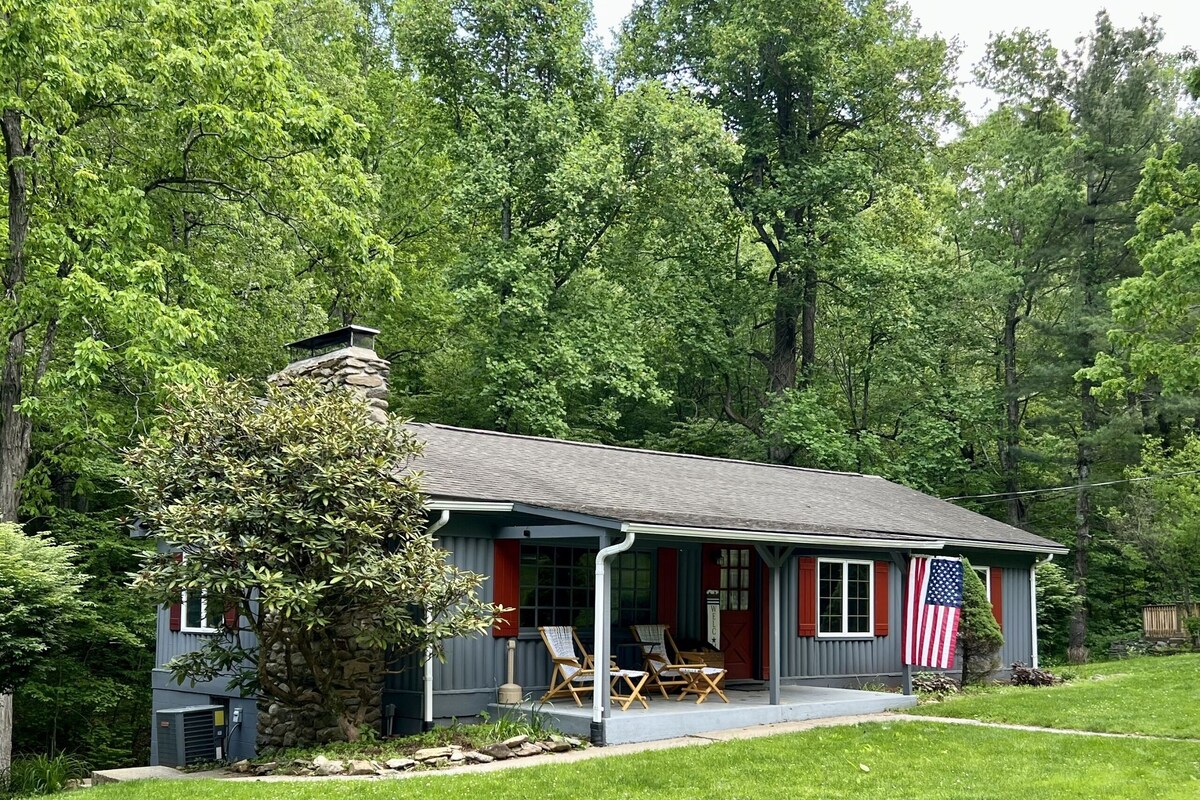 A small house with a porch, an American flag, and a stone chimney.