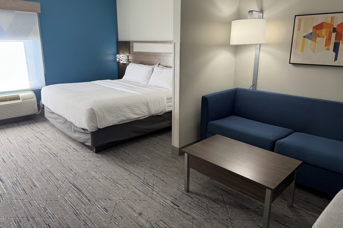 A hotel room with a bed, a blue sofa, a small table, and a lamp.