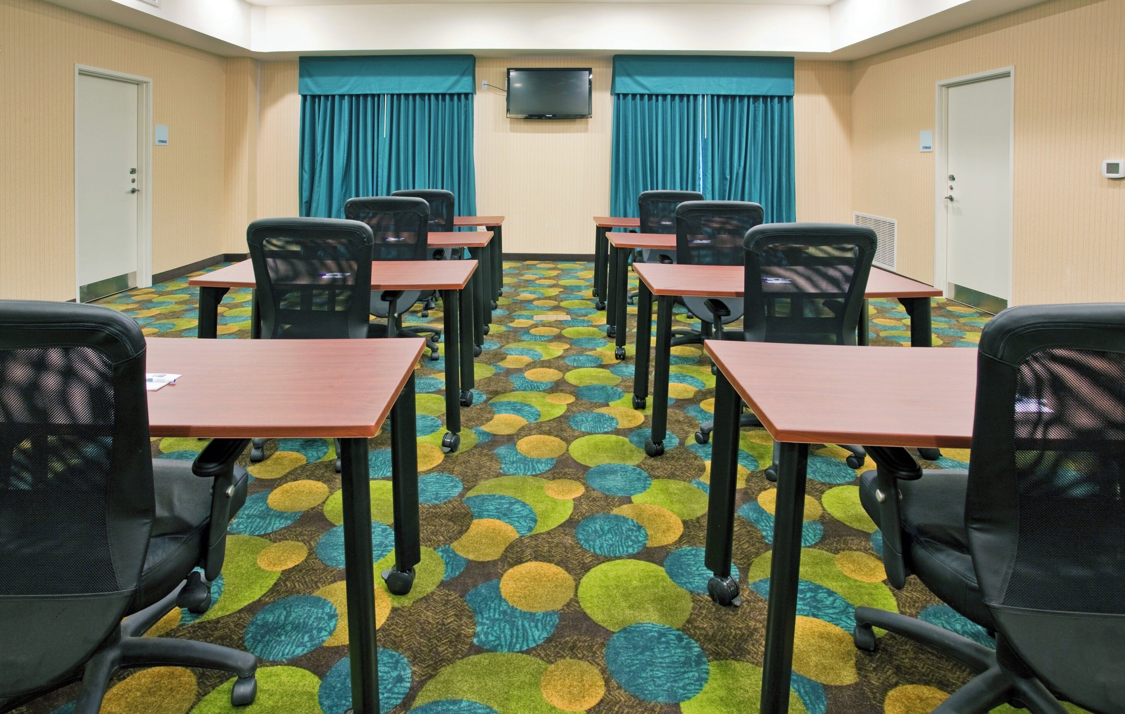 Une salle de conférence équipée de six tables et de chaises, d’un téléviseur à écran plat fixé au mur et d’un tapis à motifs.