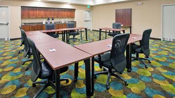 A conference room with a long table, chairs, a kitchenette, and a patterned carpet.