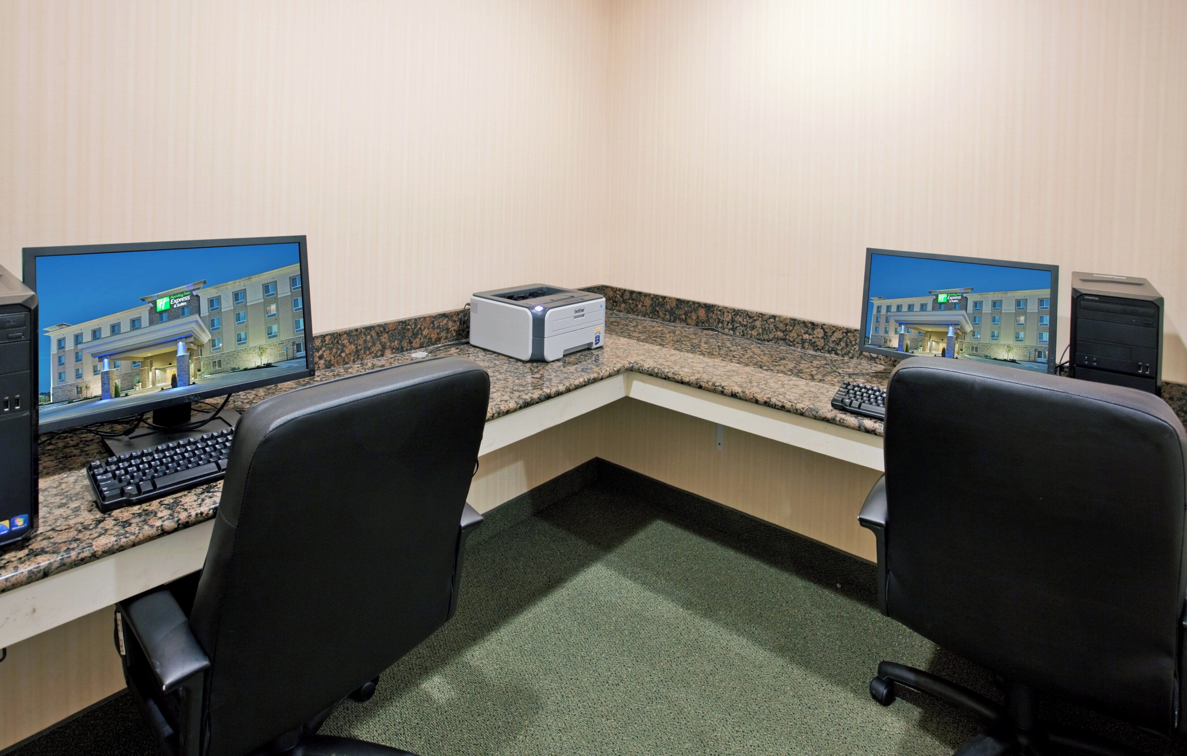 A hotel room with two desks, each equipped with a computer monitor, keyboard, and printer.