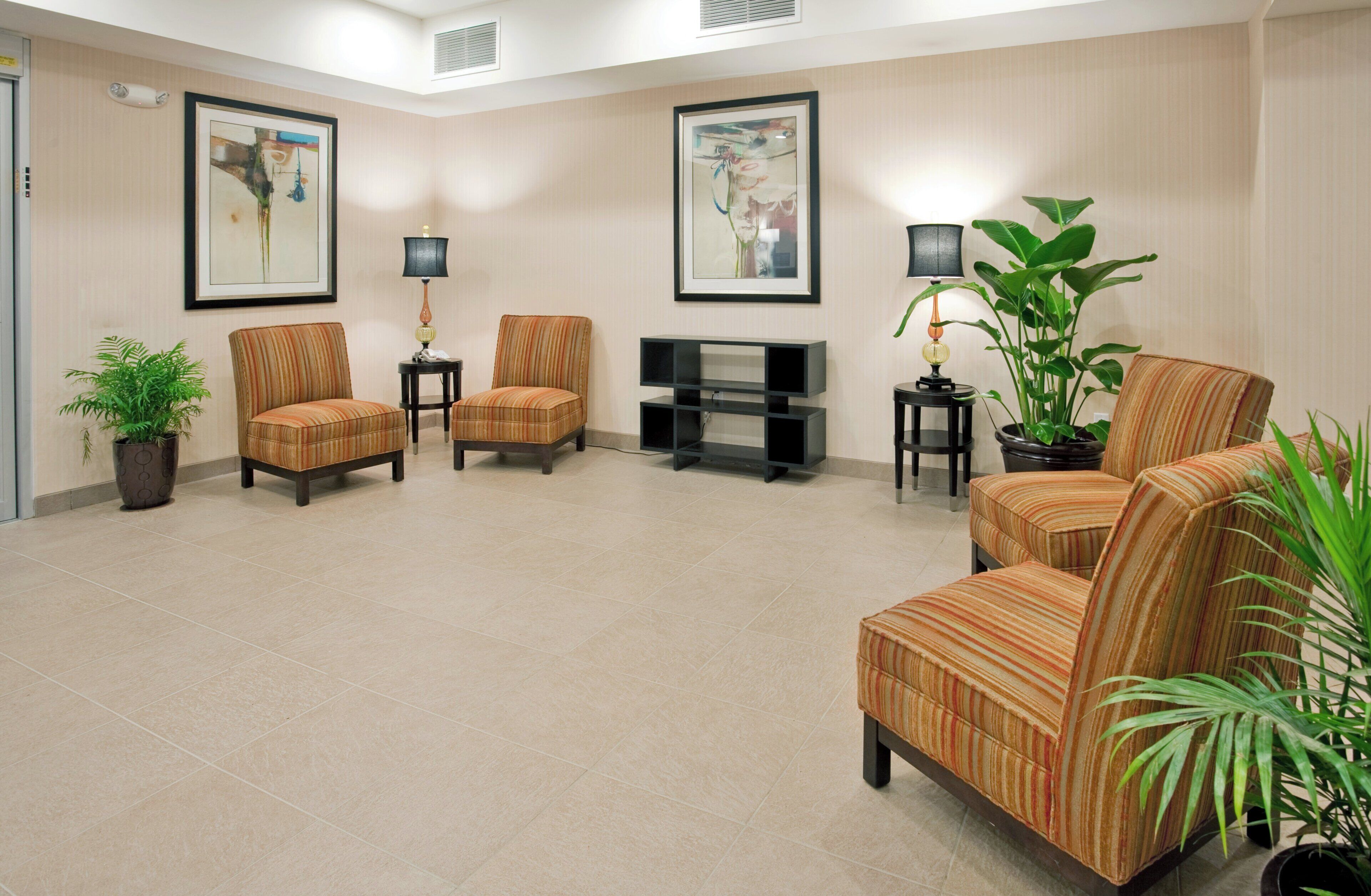 A spacious lobby with a flat-screen TV, multiple chairs, potted plants, and framed artwork on the walls.