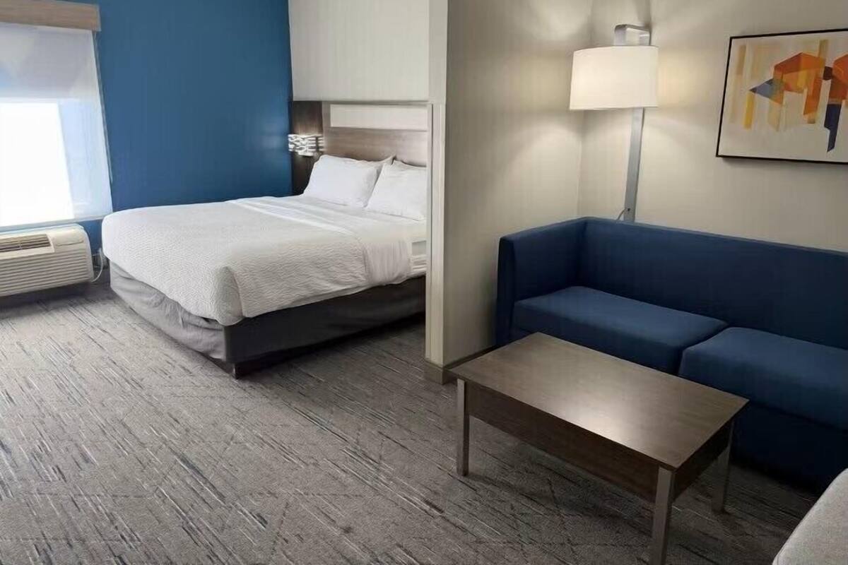 Una habitación de hotel con una cama, un sofá azul, una mesita y una lámpara.