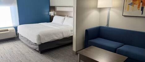 Una habitación de hotel con una cama, un sofá azul, una mesita y una lámpara.