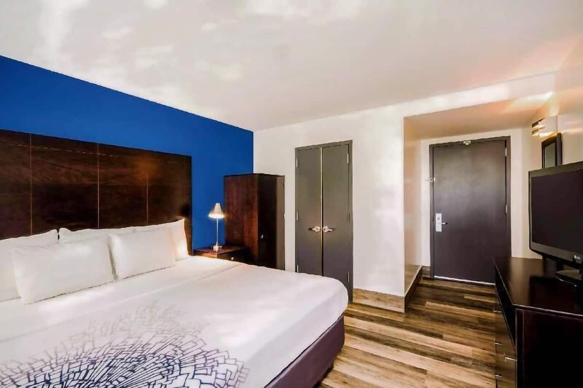 Une chambre d’hôtel avec un grand lit, une armoire, une télévision et une porte donnant sur une autre pièce.