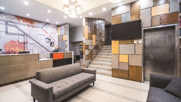 A modern hotel lobby with a reception desk, a staircase, and a sofa.