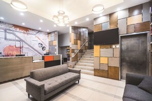 Un hall d’hôtel moderne avec un comptoir d’accueil, un escalier et un canapé.