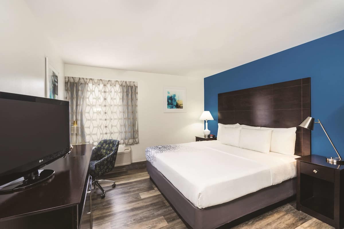 Une chambre d’hôtel avec un grand lit, un bureau doté d’un téléviseur à écran plat, une chaise, une table de chevet avec une lampe et un tableau au mur.