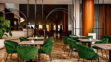 A modern hotel lobby with green velvet chairs, marble flooring, and a reception area in the background.