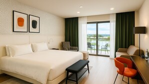 A hotel room with a large bed, a bench, a desk with a chair, and a view of a green outdoor area. - voco Nola Naples Vulcano Buono by IHG (Nola)