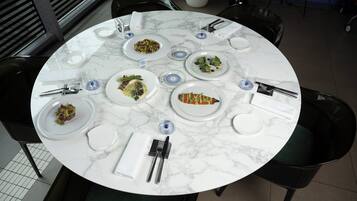 A round marble table with multiple plates of food, cutlery, and glasses.
