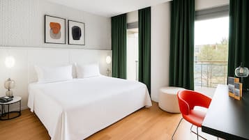 A modern hotel room with a large bed, a desk with a chair, and a view of the city.