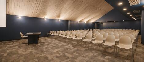 Un salón de conferencias con filas de sillas, un atril y un techo alto con vigas de madera.