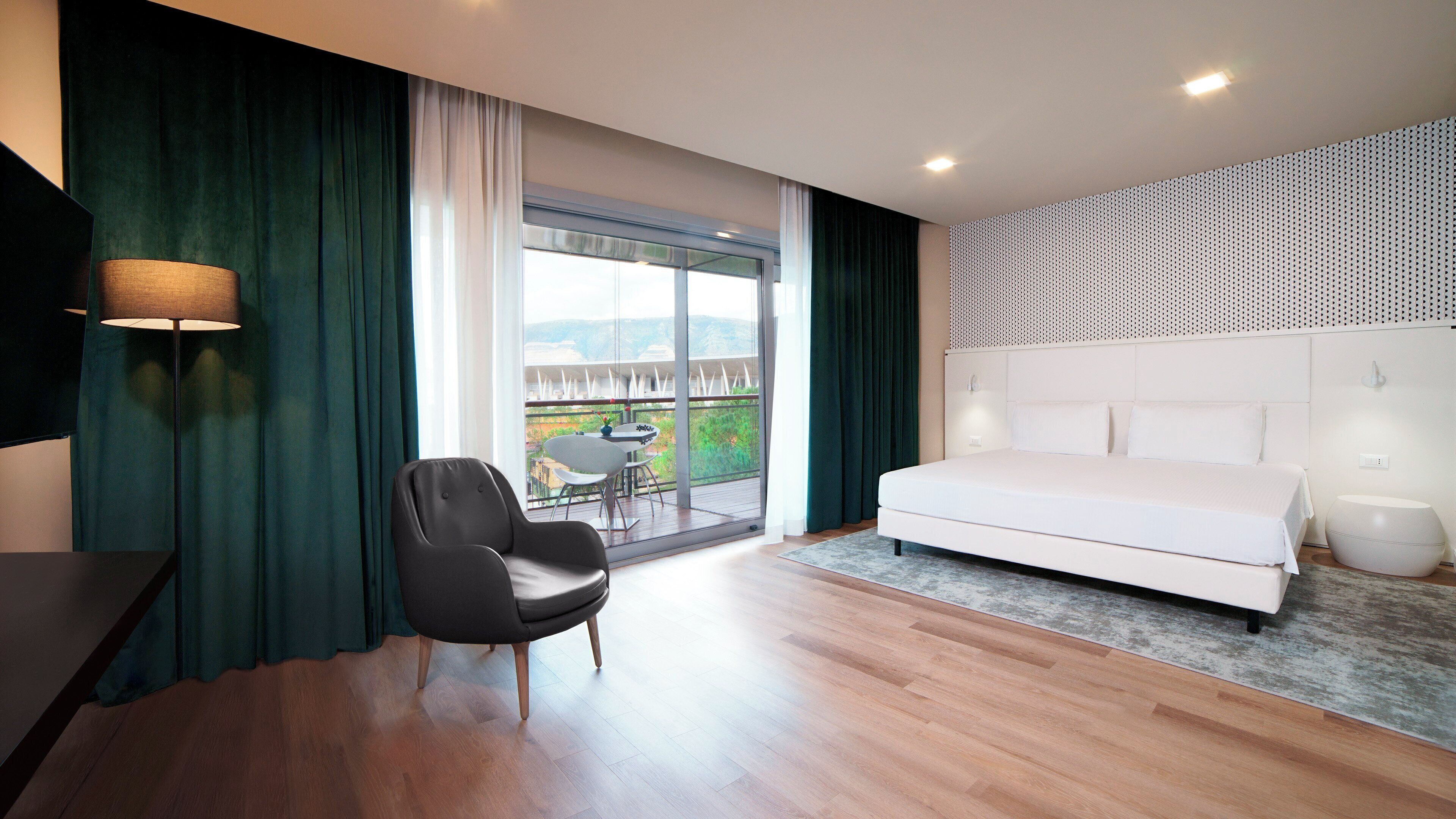 Un dormitorio moderno con una cama grande, una silla, un escritorio y un balcón con mesa y sillas.