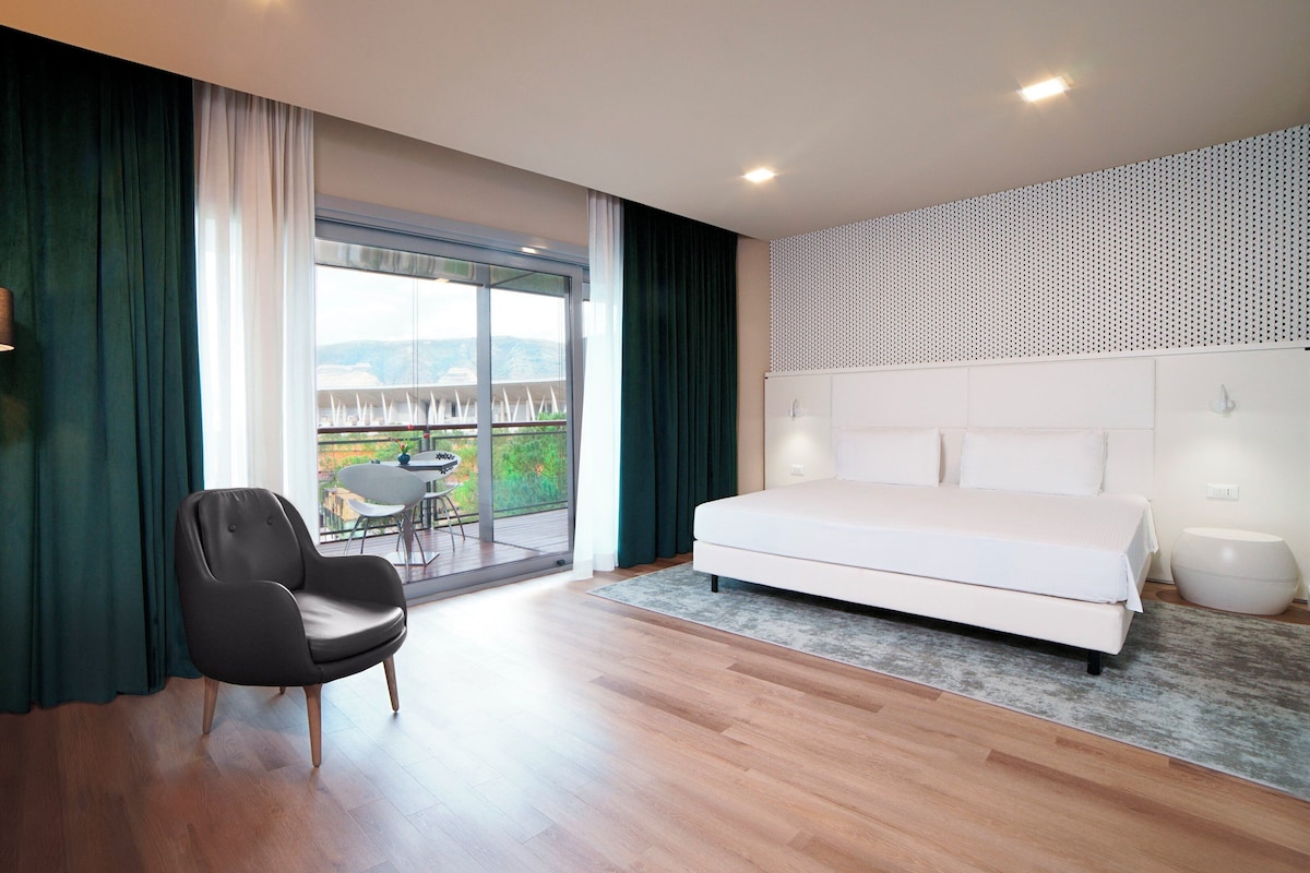 Ein modernes Schlafzimmer mit einem großen Bett, einem Sessel, einem Tisch und einem Balkon mit Blick.