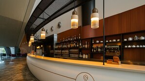A modern bar area with a curved counter, shelves with bottles and glasses, and pendant lighting. - voco Nola Naples Vulcano Buono by IHG (Nola)
