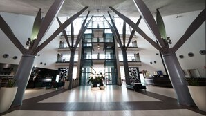Un hall d’entrée spacieux, doté de hauts plafonds et d’un design moderne, comprenant un comptoir d’accueil, des espaces de détente et de grandes plantes en pot.