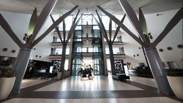 A spacious lobby with high ceilings and a modern design, featuring a reception desk, seating areas, and large potted plants. - voco Nola Naples Vulcano Buono by IHG (Nola)