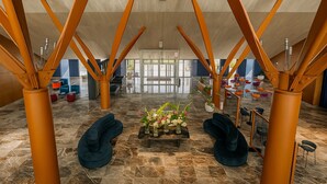 A spacious lobby with a modern design, featuring a central seating area with a floral arrangement, surrounded by orange structural columns and a marble floor. - voco Nola Naples Vulcano Buono by IHG (Nola)