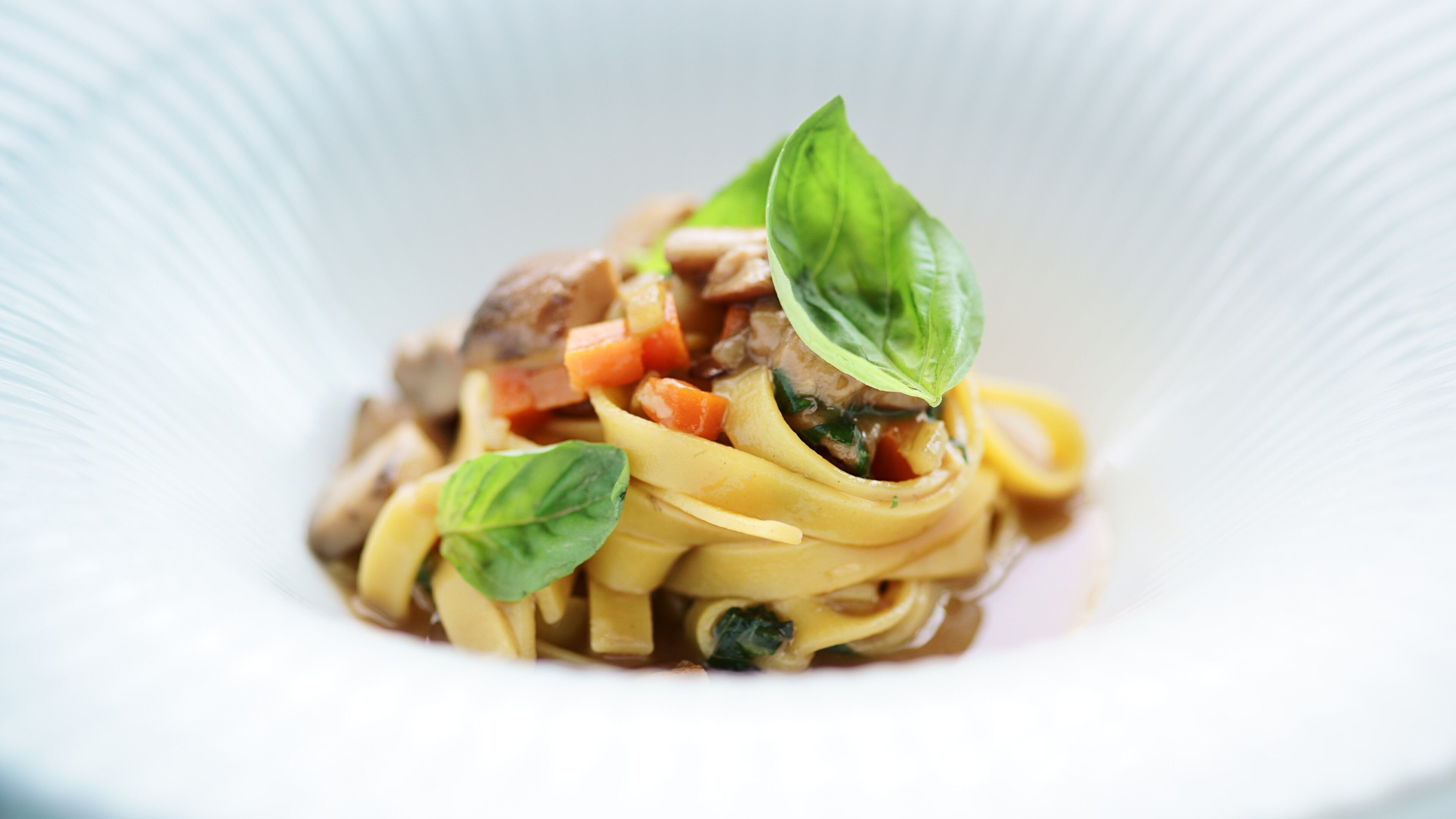 Un plato de pasta con verduras y carne, decorado con hojas de albahaca.
