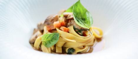 A dish of pasta with vegetables and meat, garnished with basil leaves.