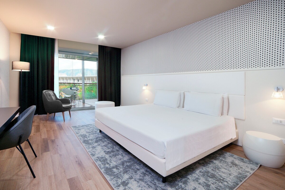 A modern hotel room with a large bed, a desk, and a TV.