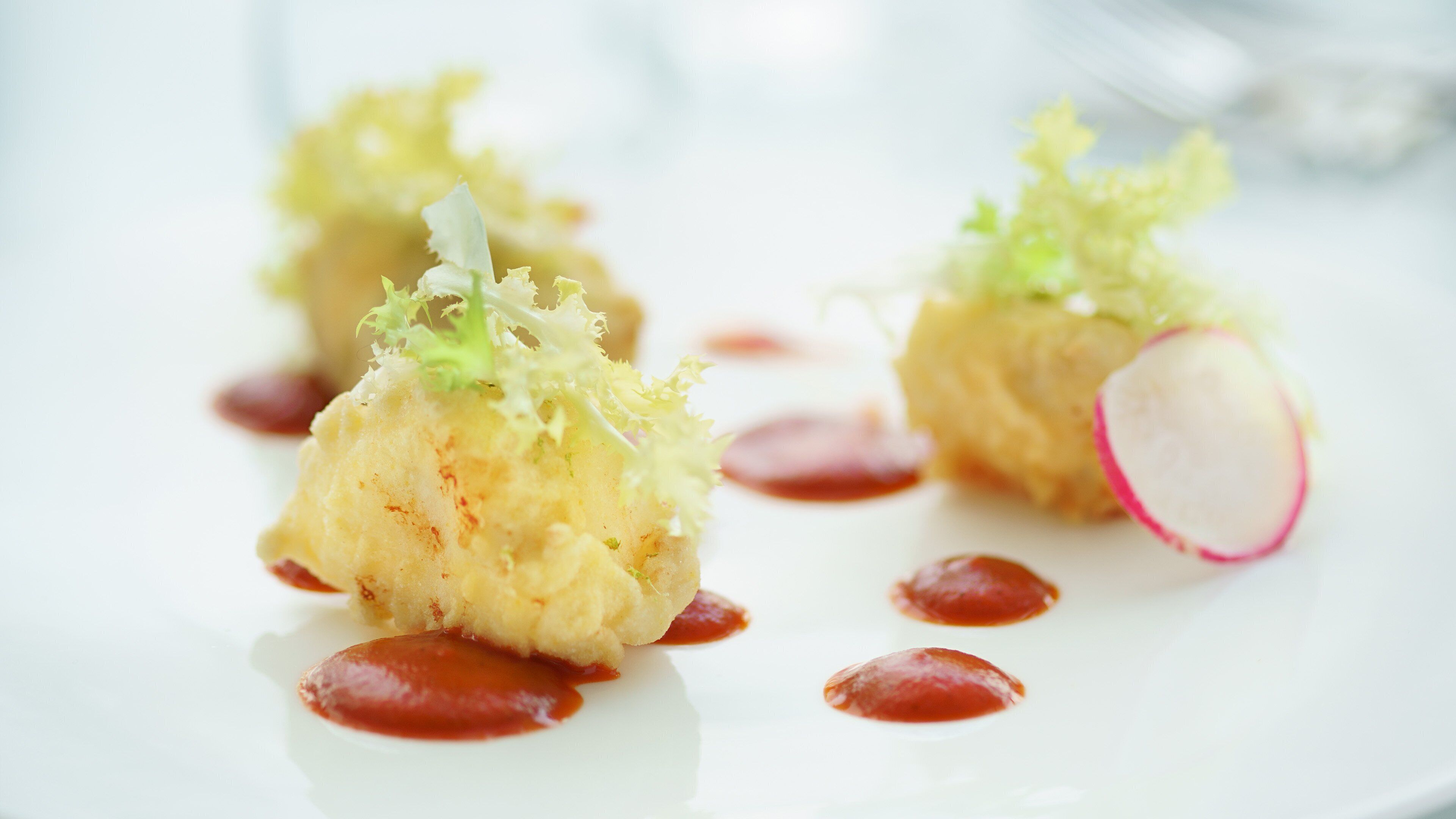 Une assiette blanche contenant divers aliments, notamment un morceau de chou-fleur garni de verdure et une tranche de radis, ainsi que quelques points de sauce rouge.