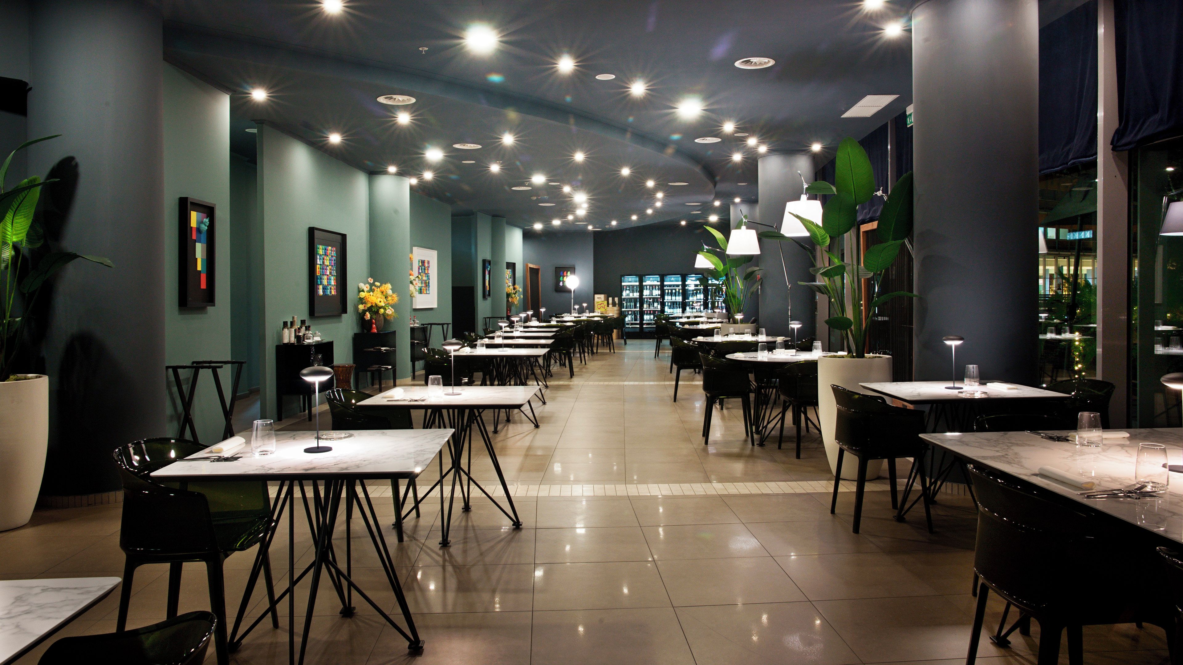 Un restaurante con varias mesas y sillas, piso de baldosas y luces en el techo.