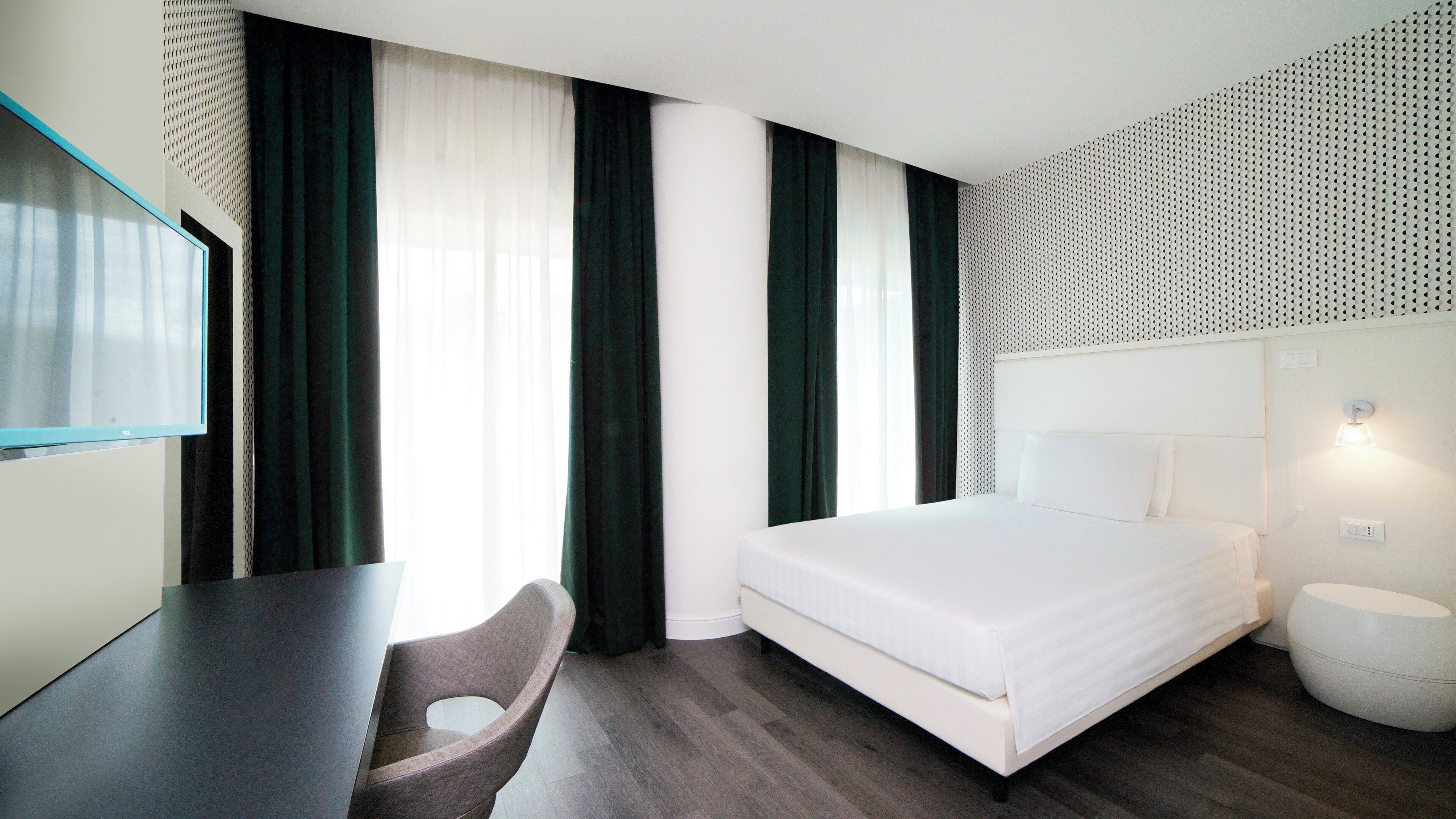 Ett modernt hotellrum med en säng, ett skrivbord och en stol.
