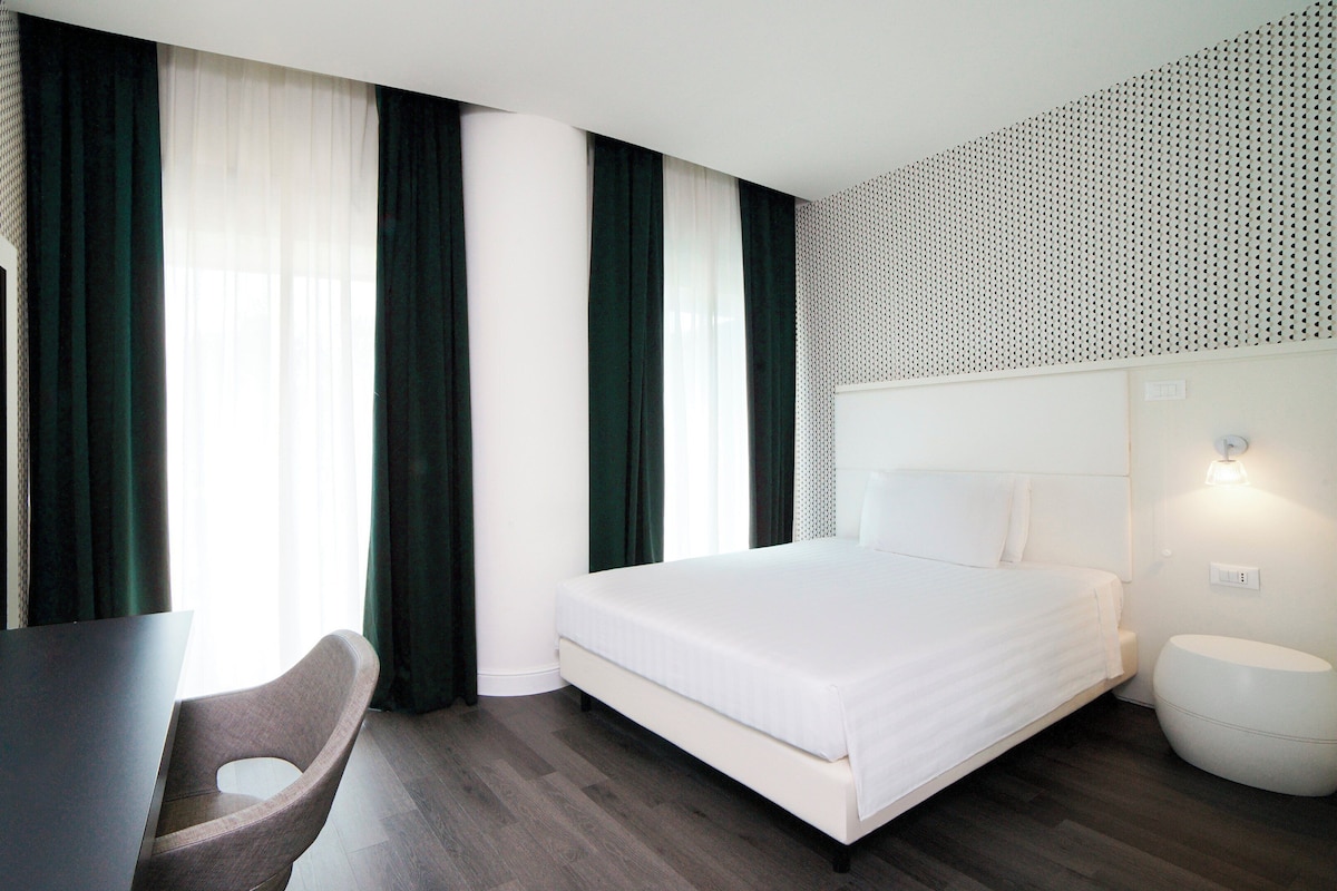 A modern hotel room with a bed, a desk, and a chair.