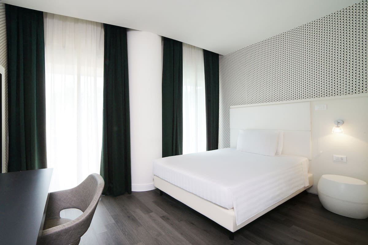 A modern hotel room with a bed, a desk, and a chair.