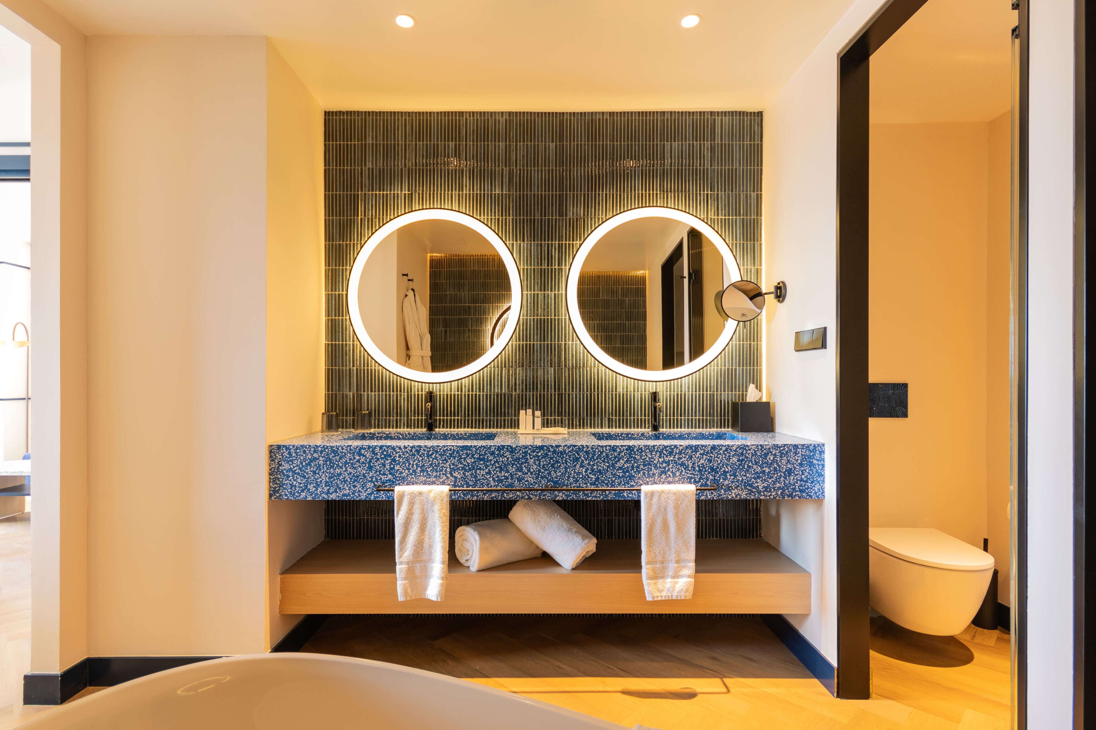 A modern bathroom with a dual mirror setup, a blue speckled countertop, and a white toilet.