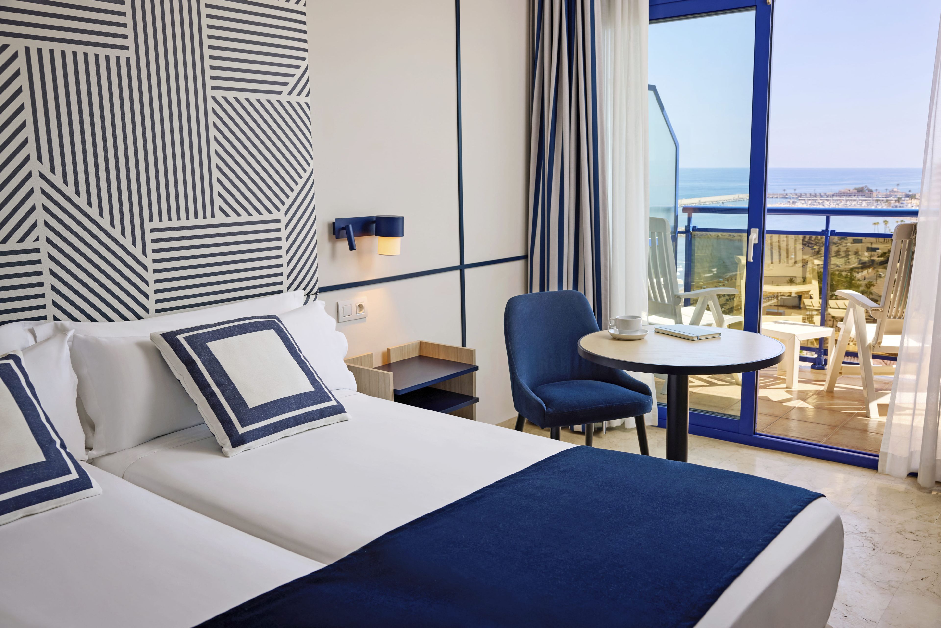 Une chambre d’hôtel avec un lit, une chaise, une petite table et une vue sur la mer.